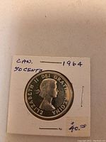Front side of 1964 Canada 50 cent coin in cardboard holder, showing Queen Elizabeth II portrait with surrounding text.