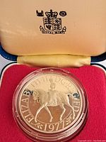 Obverse side of the 1977 Queen Elizabeth II silver proof coin featuring the Queen on horseback with inscription, housed in a protective capsule within a red velvet-lined display case.