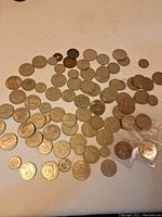 Overview photo showing about 60 assorted UK coins laid out featuring various sizes and designs mostly silver color with some discoloration and wear.
