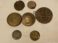 Photo showing seven assorted vintage world silver coins on a light fabric background, including larger coins with inscriptions and smaller ones, some with holes for use as pendants.
