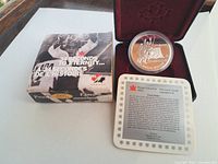 Photo showing the silver proof coin in protective capsule inside a burgundy lined black presentation case, Certificate of Authenticity, and original product box with hockey theme.