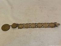 Full view of the coin bracelet laid flat, showing all linked coins including one large coin at one end and several slightly smaller coins connected by metal rings.