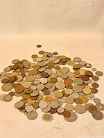 Wide view of a large assortment of mixed vintage world coins in various metals and sizes spread out on a white surface.