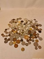 Wide shot displaying a large assortment of vintage world coins spread on a flat surface, showing variation in size, color, and condition.