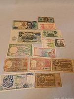 Lot of assorted vintage and antique world paper money currency, 14 notes of various denominations and countries shown on a plain surface with visible wear and signs of age.
