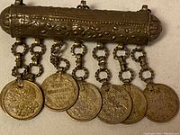 Full view of traditional jewelry with six coins dangling from ornate silver horizontal bar.