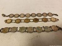 Three silver coin bracelets laid flat showing linked coin designs with various monarch portraits.