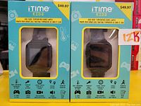 Two iTIME Kids smart watches in blue retail packaging, showing front of boxes with watch visible through clear window, listing features such as body temperature detection, games, camera, and pedometer.