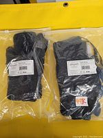 Two black fleece heat therapy gloves in sealed plastic packaging with labels visible showing brand Abco Tech and product details.