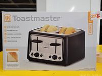 Front view of Toastmaster 4-slice toaster box showing product image and features including extra wide slots, high-rise toast lift, adjustable shade control, bagel toasting function, and defrost function.