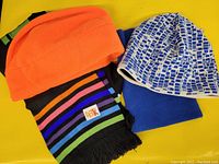 Photo showing black scarf with colorful stripes, orange fleece toque, white-and-blue patterned toque, blue stretchy neck warmer, and matching colorful striped toque.