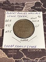 Obverse side of copper half penny token showing store name 'Robert Purves Cheap Family Store Wallace' mounted in cardboard holder with handwritten notes indicating item details.