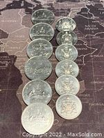 Twelve Canadian coins arranged in two rows on a world map surface, showing the obverse and reverse sides with various commemorative and national designs.