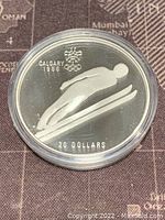 Front side of silver coin showing ski jumper design, Calgary 1988 Winter Olympics emblem, and denomination.