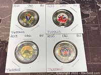 Four Canadian twoonie coins with colorized designs in holders showing year and condition