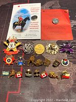 Photo showing all 22 assorted pins laid out on a dark surface with a map design background, featuring the two Royal Canadian Mint sterling silver commemorative pins with their certificates and various other colorful pins including Disney and Canadian-themed pins.