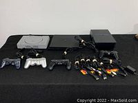 Top-down view of all three PlayStation consoles with four controllers and multiple AV cables laid on black cloth.