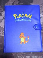Blue Pokémon trading card binder with Charmander on front cover, closed with snap clasp.