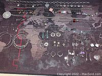 Full spread view of assorted silver tone jewelry including necklaces, bracelets, earrings, and hoops laid out on dark map background
