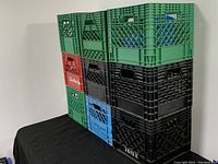 Nine assorted plastic storage and moving crates stacked in three columns and three rows against a white background, showing a variety of colors and branding.