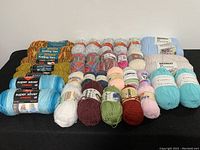 Front view of assorted yarn skeins including blues, greens, multicolor, and white on black surface
