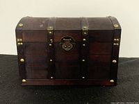 Front view of small wooden chest with metal accents and latch, showing detailed metal rivets and latch.
