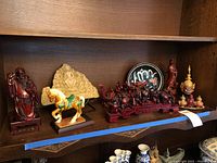 Shelf displaying multiple Asian-themed figurines including lacquered statues, stone carving, ceramic horse, plate, and incense burners