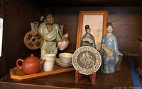 Photo showing all ceramic figurines, framed wall art, decorative plate, tea pot with cups and saucers on wooden tray