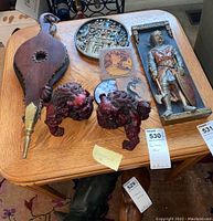 Wide view of the lot items arranged on a wooden table: two red Foo Dog figurines, fireplace bellows, coasters, and multiple plaques.