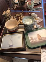 Overview of brass nautical decor, ceramic pieces, horse figurine, framed art, model plane, and other items on table.