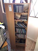 Wooden storage shelf with multiple shelves filled with music CDs, placed near window.