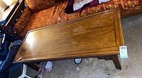 Full view of wood coffee table placed in front of a patterned red couch showing the rectangular top and leg design.