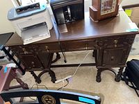 Front angle of vintage wooden desk showing drawers, cabinets, brass hardware and carved leg details