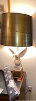 Overall view of the eagle lamp with its metallic gold lampshade and the folded flag beside it on a table.