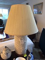 Full view of lamp with cream pleated shade sitting on a small wooden table, showing overall height and setting.