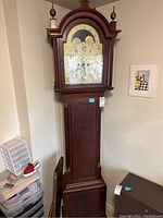 Full front view of tall clock showing arched bonnet, brass finials and dial