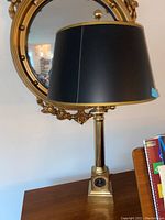 Table lamp with black shade and gold-toned column base with United States Air Force emblem plaque on base.