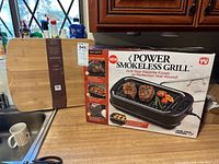 Photo showing boxed Power Smokeless Grill and bamboo carving board on kitchen counter.