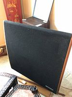 Front view of one speaker showing black fabric grille and walnut veneer side panels