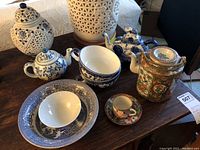 Overview of all ceramic and porcelain items on table: multiple teapots, bowls, plates, a teacup, and a decorative jar