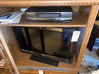 Photo showing Vizio VL260M TV and Panasonic VHS player placed in a wooden entertainment shelf.
