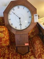 Front view of the vintage wooden wall clock with octagonal frame, white dial with Roman numerals, and brass bezel.
