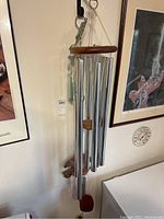 Front and side views of three metal and wood wind chimes showing metal tubes and wooden components including wooden top platforms and wooden wind catchers, hung on a hook.