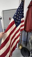 American flag held to show the stars and stripes pattern, with wooden pole and metal base visible.