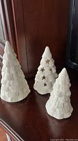 Three white snowy textured Christmas tree figurines, one with star cutouts visible, on wood surface