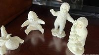 Four Department 56 Snow Babies figurines arranged on a wood surface, showing various poses and textured white snowsuits