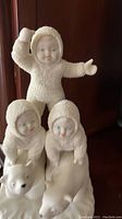 Photo showing three Departments 56 Snowbabies figurines in white textured suits, two on polar bears and one standing, highlighting details of the faces and costumes.