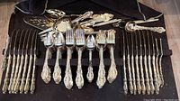 Full layout of all cutlery and utensils showing gold plated handles with ornate pattern. Set includes knives, forks, spoons, and serving pieces.