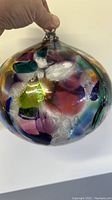 Photo of large multi-color glass ornament showing various colored patches with a clear hanging loop.