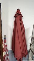 Folded large maroon patio umbrella canopy hanging against a white wall.